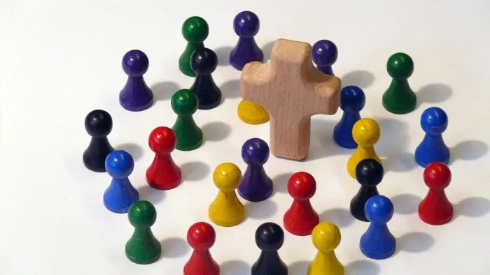 Holzfiguren in verschiedenen Farben um ein hölzernes Kreuz angeordnet