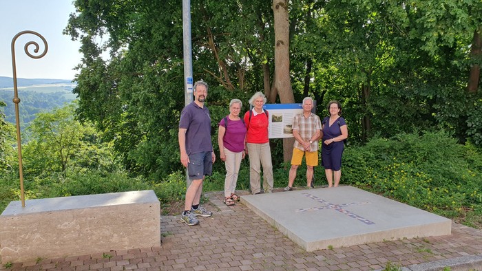 Eine Gruppe von fünf Personen, die in einer üppigen Außenanlage in der Nähe einer Gedenktafel und dekorativer Steinelemente posieren.
