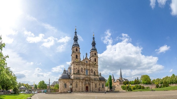 Imposante Kathedrale mit Zwillingstürmen vor strahlend blauem Himmel und üppiger grüner Umgebung.