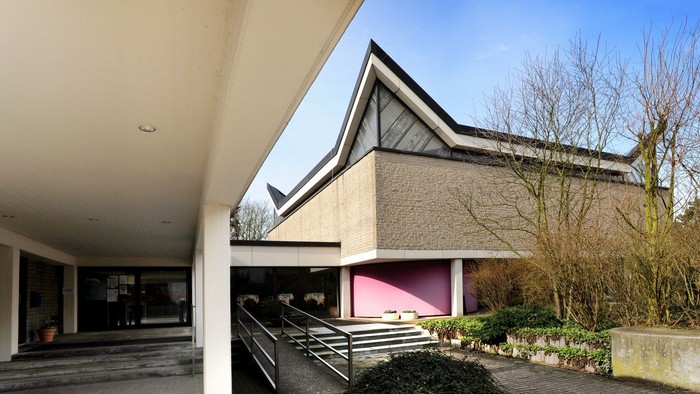 Modernes Gebäude mit schrägem Dach und pinkfarbenem Innenraum, der durch offene Türen sichtbar ist