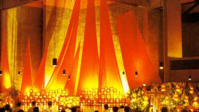 Ein religiöses Treffen mit vielen Menschen in weißen Kleidern, die in einem Raum mit orangefarbenem Licht und vielen Kerzen sitzen