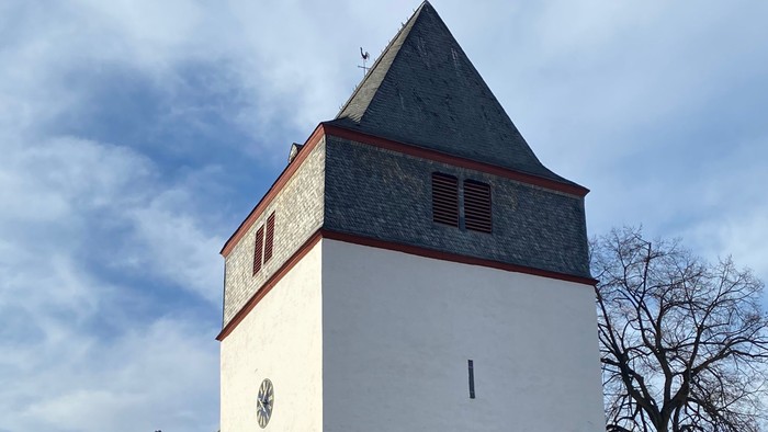 Weißer Kirchturm mit spitzem Dach und kleinem Fenster