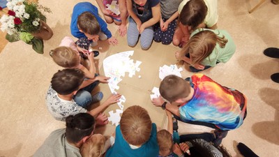 Ein Kreis von Erwachsenen und Kindern spielt gemeinsam auf dem Boden.