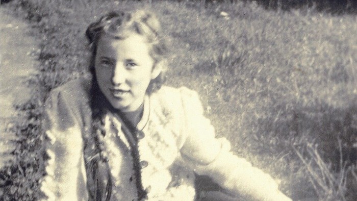 Junges Mädchen sitzt im Gras und lächelt.