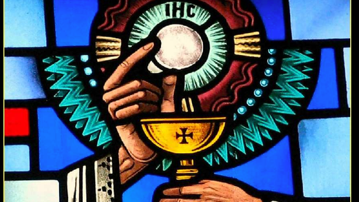 Farvet glasafbildning af en hånd, der holder et alterbæger under en religiøs nadverceremoni.