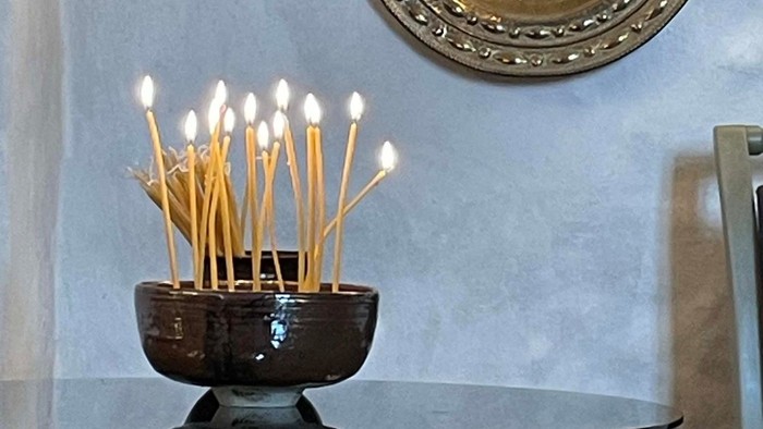 En skål med røgelsespinde står på et bord under en dekorativ vægplade.