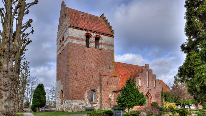 Historisk murstenskirke med et højt tårn og buede vinduer i en rolig, anlagt kirkegård.