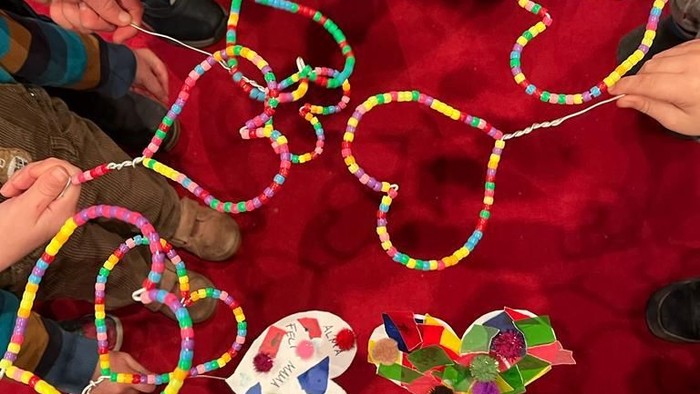 Kinder, die bunte Perlenherzen und Papierdekorationen auf einer roten Oberfläche basteln.