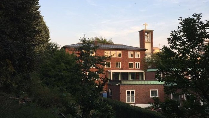 Et rødt teglsteinshus med klokketårn og træer foran