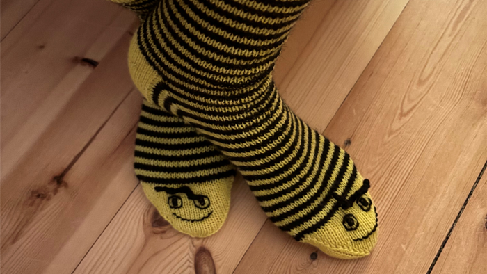 En person med strimlet bjørnesokker står på trægolv.