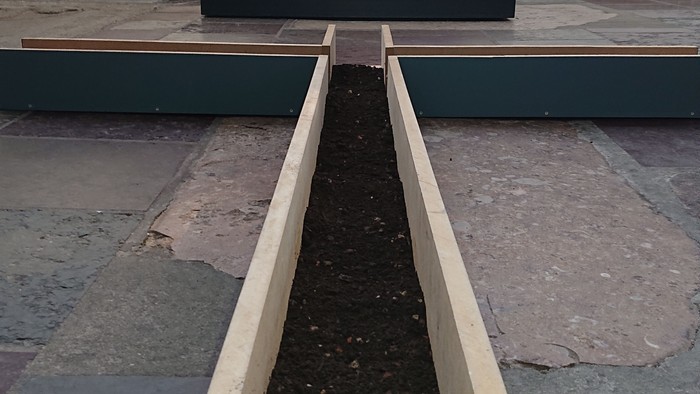 Ein Holzrahmen mit schwarzer Substanz darin vor einem abstrakten Gemälde.