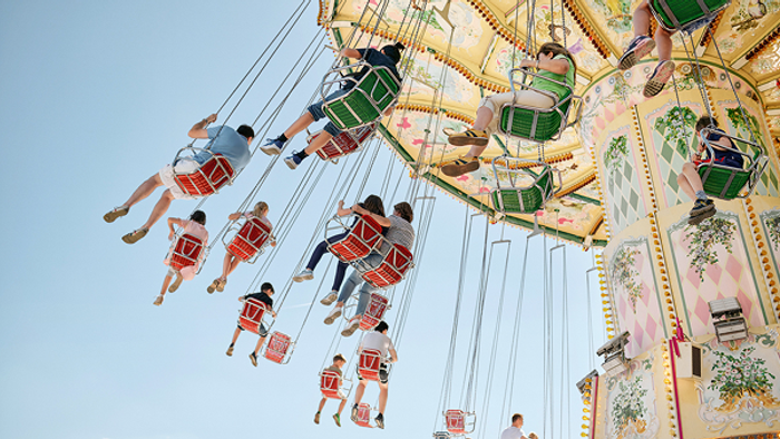 Bunter Schaukelkarussell mit Fahrgästen, die eine fröhliche, kopfüber Fahrt unter strahlendem Himmel genießen.