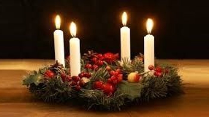 En adventskranse med fire lysende lys og grønne blomster på træbord.