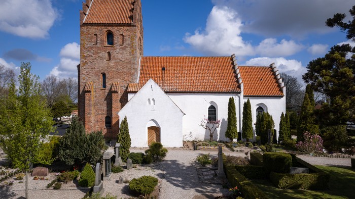 En malerisk hvid kirke med et højt murstens tårn placeret i en fredfyldt, anlagt kirkegård.
