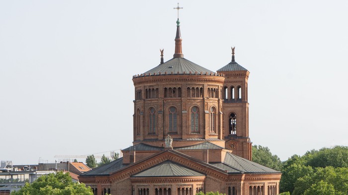 Große Ziegelkirche mit zwei Türmen und spitzen Dächern, umgeben von Bäumen