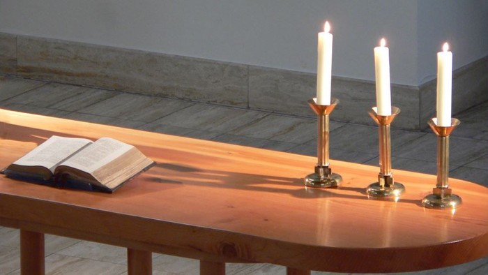 Drei brennende Kerzen auf einem Holztisch mit zwei Büchern