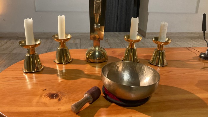 Heiliger Altaraufbau mit Kerzen, einer Messing-Klangschale und einem Kruzifix auf einem Holztisch.