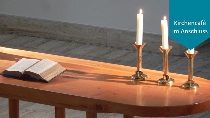 Ein Holztisch mit zwei brennenden Kerzen und einem aufgeschlagenen Buch im Kirchencafé im Anschluss
