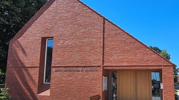 Rote Backsteinkirche mit Holztüren und Fenster, Bank davor, blauer Himmel