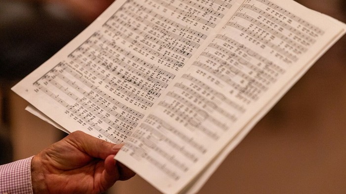 Eine Hand hält ein aufgeschlagenes Buch mit Noten.