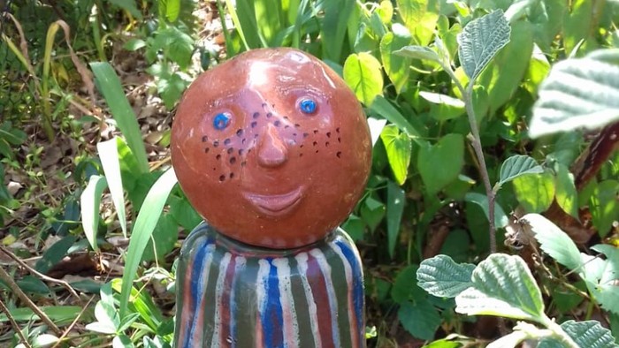 Eine rote Figur mit gestreifter Jacke steht im Garten.