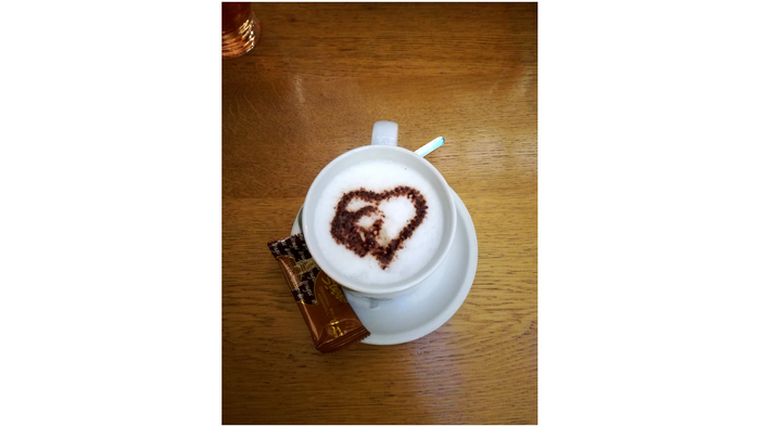 Eine Tasse Kaffee mit Herzmuster auf dem Schaum und einem Löffel daneben