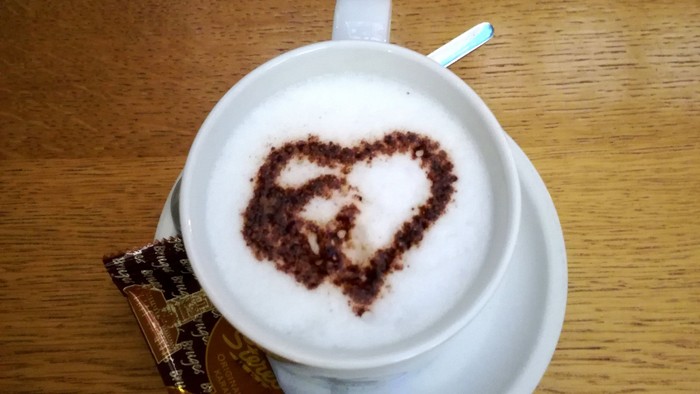 Eine Tasse Kaffee mit Herzmuster auf dem Schaum und ein Schokoladenriegel daneben
