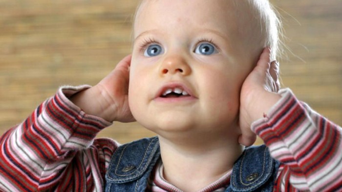 Baby mit Händen an den Ohren, das überrascht schaut.