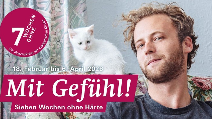 Ein Mann sitzt vor einem gemusterten Vorhang mit einer weißen Katze auf seiner Schulter