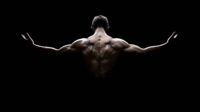 Ein muskulöser Mann mit ausgebreiteten Armen vor schwarzem Hintergrund