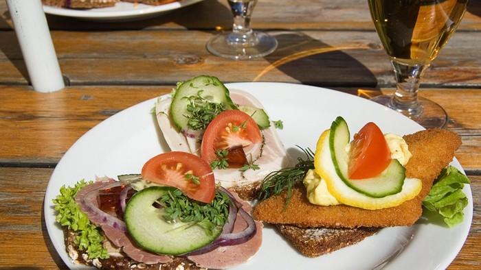 En ret med tre smørrebrød med tomater, agurker og kødslag på brød.