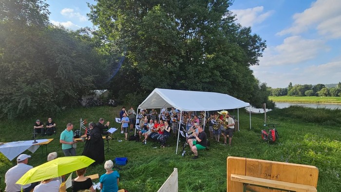Open-Air-Treffen unter einem Zelt mit Menschen, die sich unterhalten, essen und in einer grünen, malerischen Umgebung entspannen.