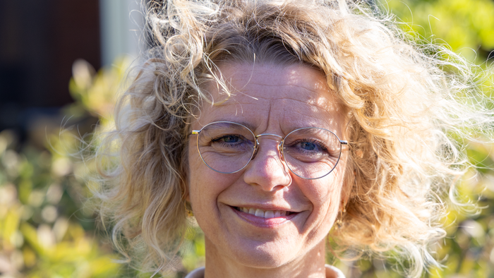 En kvinde med kurve hår og briller smiler til kameraet.