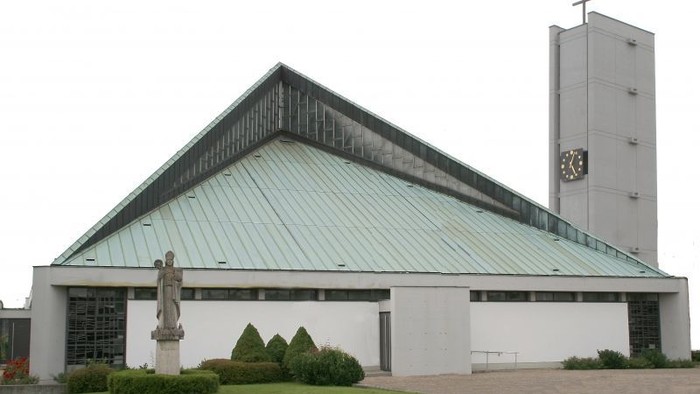 Das Bild zeigt eine moderne Kirche mit grünem Dach und hohem Turm.