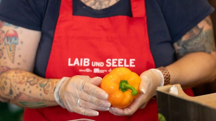 Person hält eine gelbe Paprika, trägt eine rote Schürze und Handschuhe.