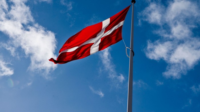 Dansk flag vimpler i bløgt vind mod et klart himmel.