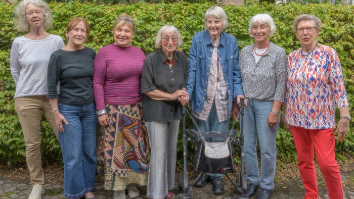 Sieben ältere Frauen stehen gemeinsam im Freien, lächeln und posieren für ein Gruppenfoto.