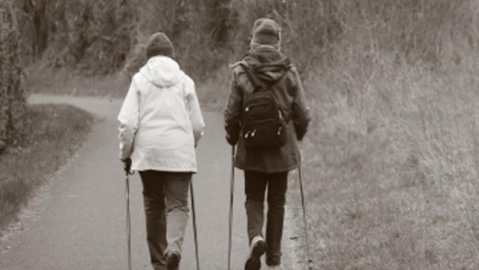 Zwei Personen gehen mit Wanderstöcken auf einem Pfad.