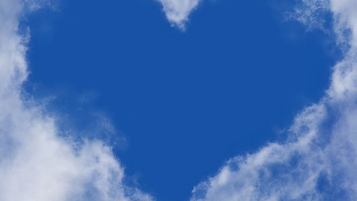 Ein herzförmiger Ausschnitt des blauen Himmels, umrahmt von flauschigen weißen Wolken, bildet ein friedvolles natürliches Herz.