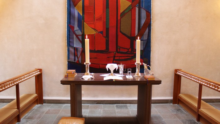 En lille kapel med alter med to lysstaker og et maleri på veggen.