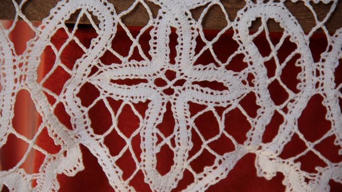 Hvidt nærbillede af kniplet kors fra alterdugen med rød baggrund