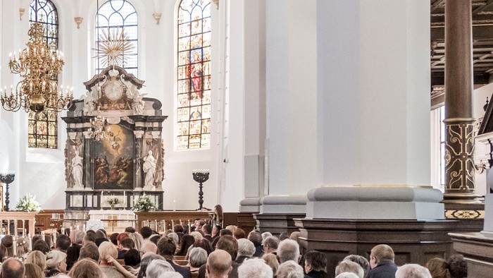En kirke med en stor samling af mennesker, der deltager i en religiøs ceremonie foran alteret.