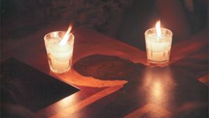 Zwei brennende Kerzen auf einem dunklen Holztisch.