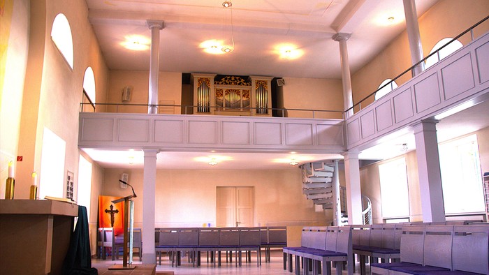 Moderne Kircheninnenraum mit Kirchenbänken, erhöhter Kanzel, Orgel und offenem architektonischem Design.