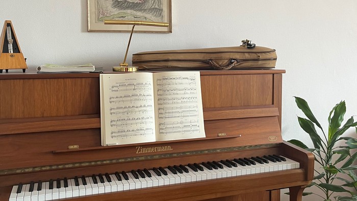 Elegantes Holzklavier mit Notenblättern, gerahmten Kunstwerken und einer kleinen Topfpflanze in der Nähe.