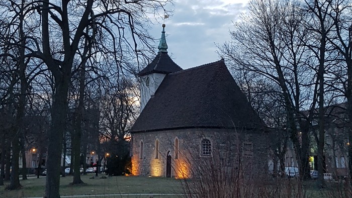 Kirche mit Turmspitze und kahlen Bäumen in der Abenddämmerung.
