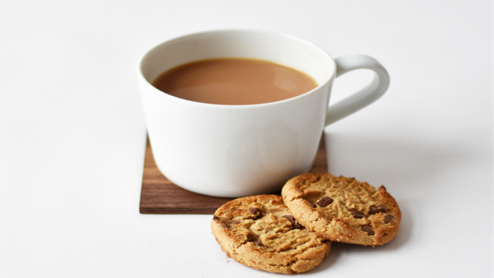 A white cup of coffee next to two cookies on a wooden coaster