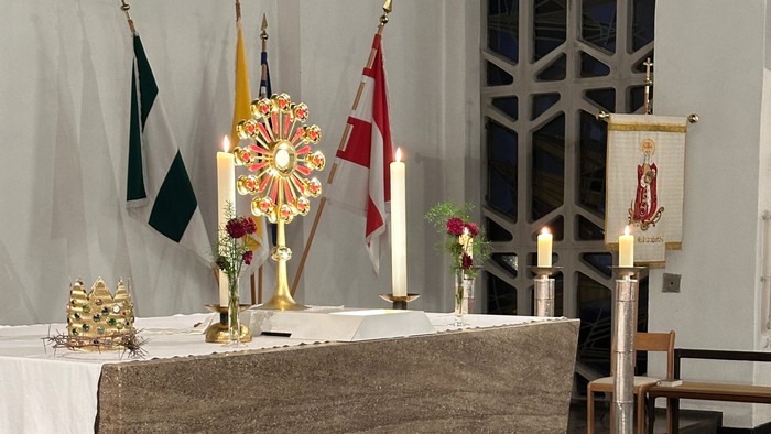 Eleganter Kirchenaltar, geschmückt mit Kerzen, Fahnen, Blumengestecken und religiösen Verzierungen auf einem Marmorboden.