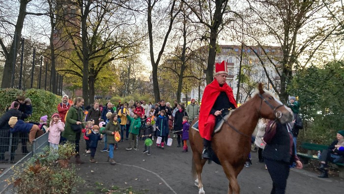 Person in Rotem Anzug reitet Pferd durch Park, viele Menschen schauen zu