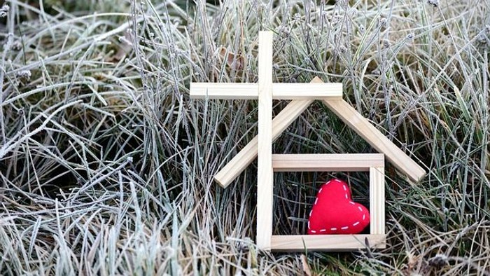 Kleines Holzhaus mit einem roten Herzen im frostigen Gras.